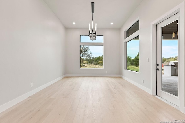 spare room with a chandelier and light wood-type flooring