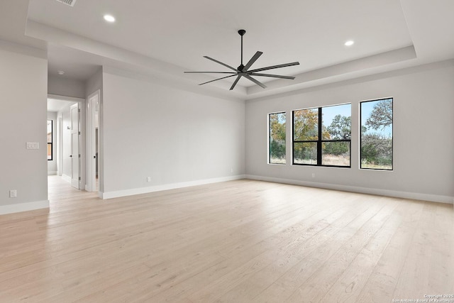 empty room featuring ceiling fan, a tray ceiling, and light hardwood / wood-style flooring