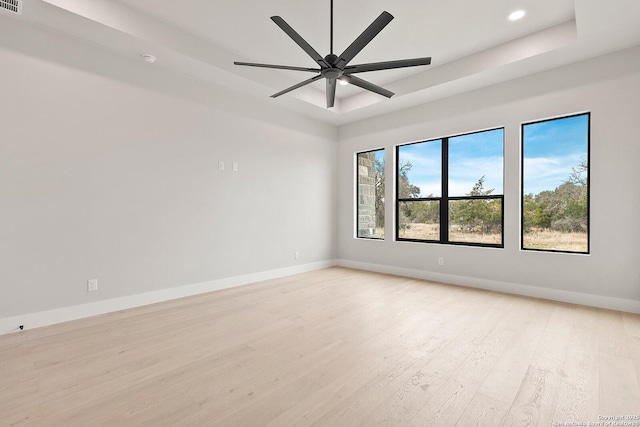 empty room featuring ceiling fan, a tray ceiling, and light hardwood / wood-style flooring