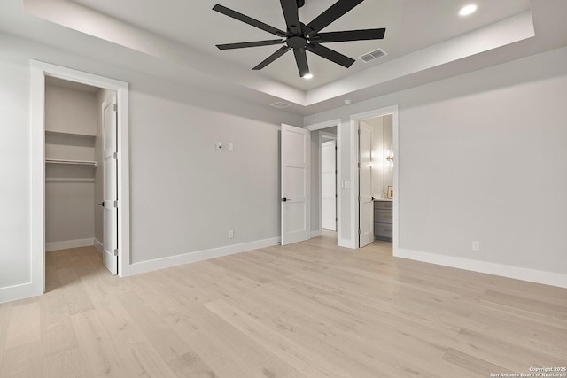 unfurnished bedroom featuring a raised ceiling, ensuite bath, ceiling fan, and a spacious closet