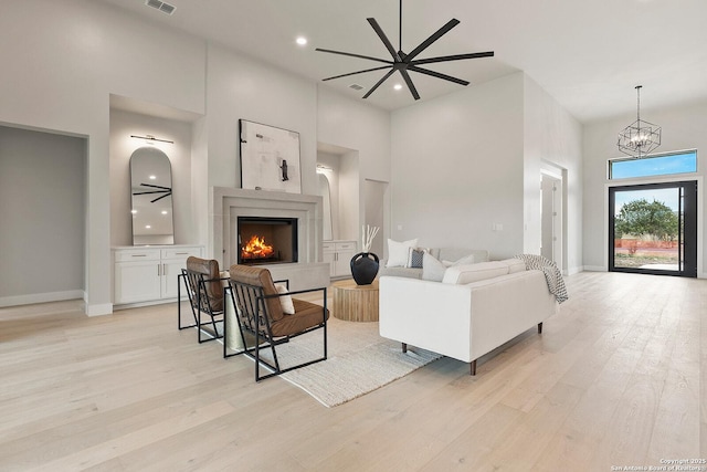 living room featuring a high ceiling, ceiling fan with notable chandelier, and light hardwood / wood-style flooring