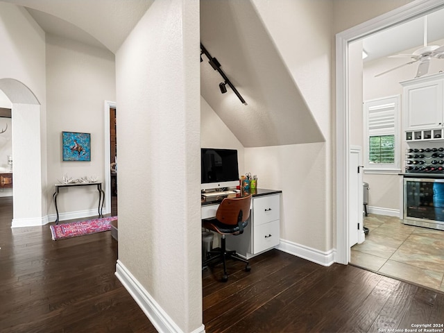 office space featuring vaulted ceiling, wine cooler, built in desk, ceiling fan, and hardwood / wood-style flooring