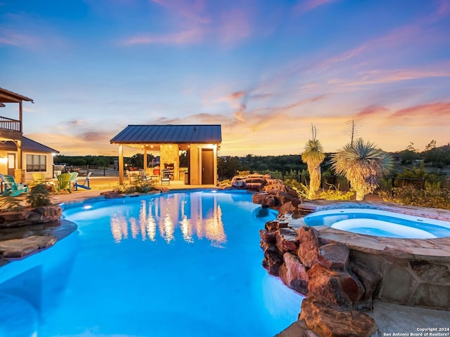 pool at dusk featuring an in ground hot tub and a patio