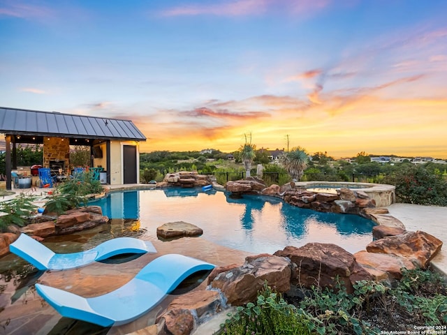 pool at dusk with a gazebo, exterior fireplace, and an in ground hot tub