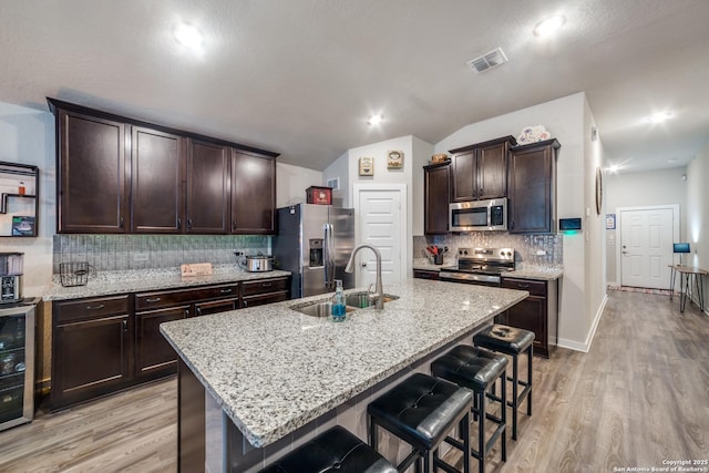 kitchen featuring light stone counters, vaulted ceiling, stainless steel appliances, a kitchen island with sink, and sink