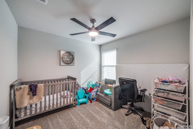 carpeted bedroom with ceiling fan and a crib