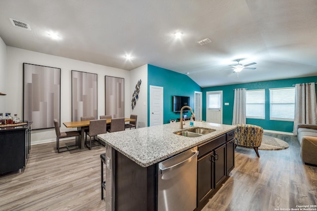 kitchen with sink, vaulted ceiling, dishwasher, light wood-type flooring, and a center island with sink