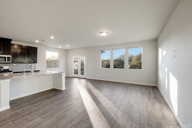 kitchen with light stone counters, tasteful backsplash, dark brown cabinetry, appliances with stainless steel finishes, and sink