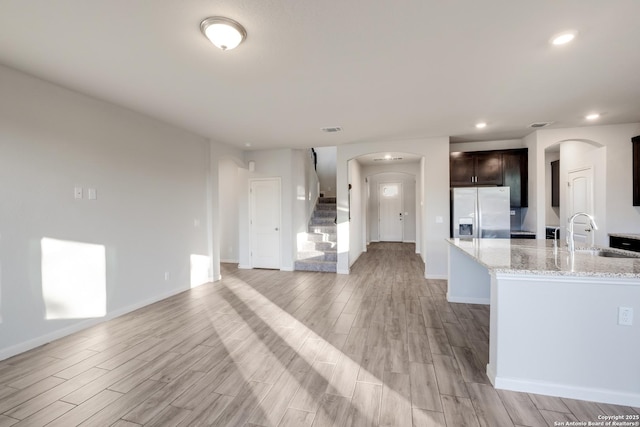 kitchen with a center island, light stone countertops, stainless steel fridge, sink, and dark brown cabinets