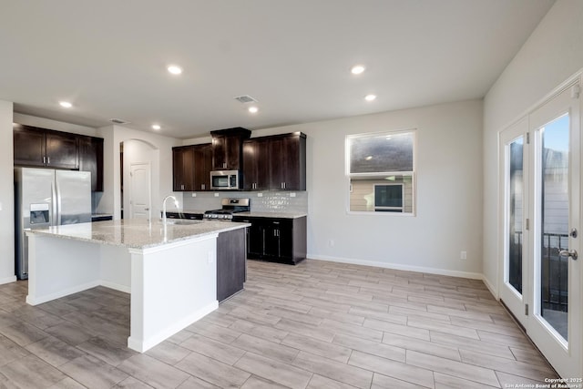 kitchen featuring a center island with sink, appliances with stainless steel finishes, light stone counters, decorative backsplash, and sink