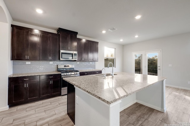 kitchen featuring sink, stainless steel appliances, a kitchen island with sink, and light stone counters