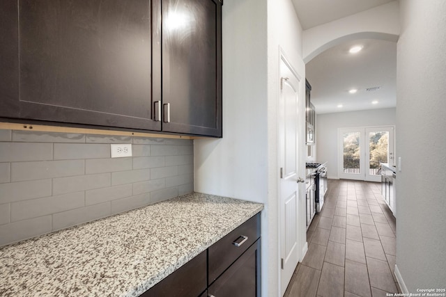 kitchen featuring high end range, light stone counters, french doors, backsplash, and dark brown cabinetry