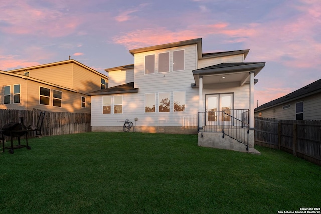 back house at dusk featuring french doors and a yard