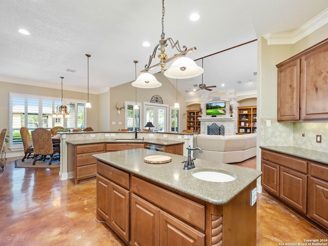 kitchen with sink, a fireplace, backsplash, hanging light fixtures, and a center island with sink