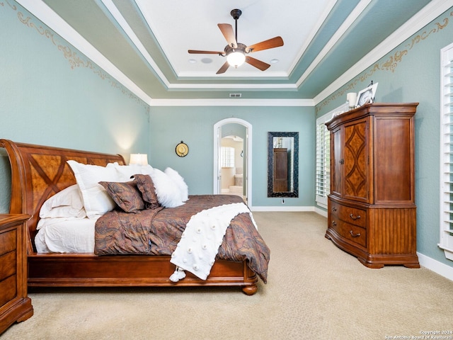 carpeted bedroom with ensuite bath, ceiling fan, a tray ceiling, and ornamental molding