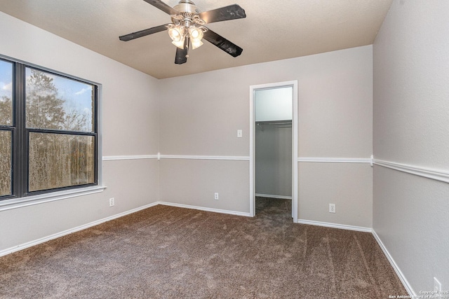 unfurnished bedroom featuring dark carpet, a closet, ceiling fan, and a spacious closet