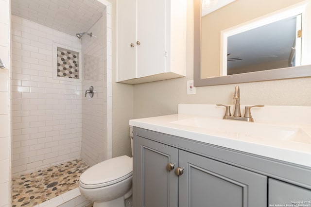 bathroom with toilet, a tile shower, and vanity