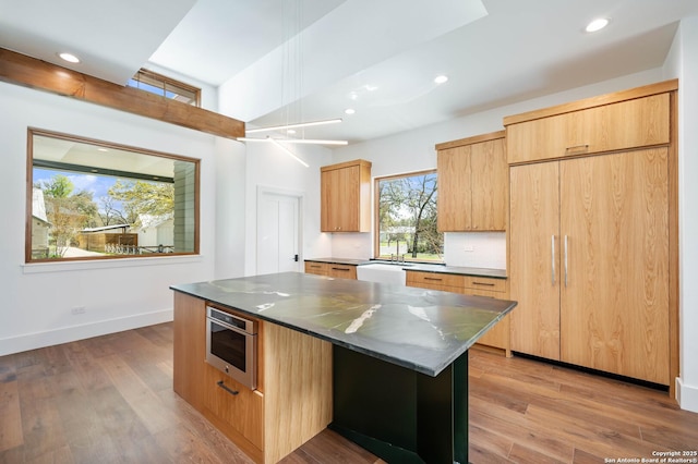 kitchen featuring oven, light wood-type flooring, dark stone countertops, and a center island