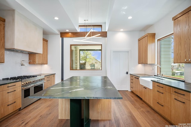 kitchen with double oven range, light hardwood / wood-style floors, a kitchen bar, a large island, and sink