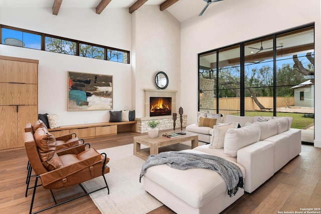 living room with a towering ceiling, beam ceiling, ceiling fan, and wood-type flooring