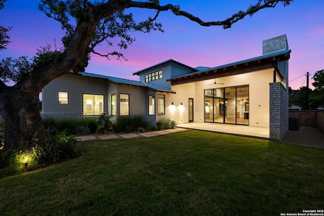 back house at dusk with ceiling fan, a patio, and a lawn