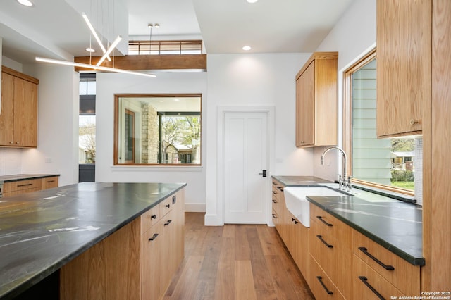 kitchen featuring light hardwood / wood-style flooring, hanging light fixtures, backsplash, dark stone counters, and sink