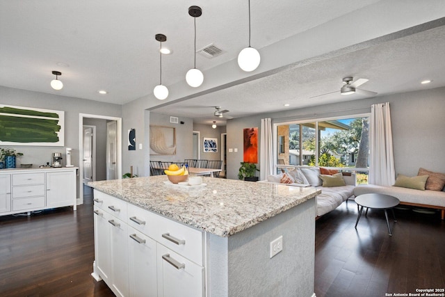 kitchen featuring a kitchen island, light stone counters, hanging light fixtures, and white cabinetry