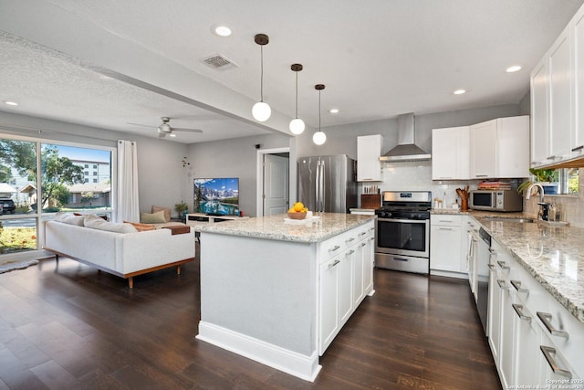 kitchen featuring stainless steel appliances, wall chimney range hood, white cabinets, and pendant lighting