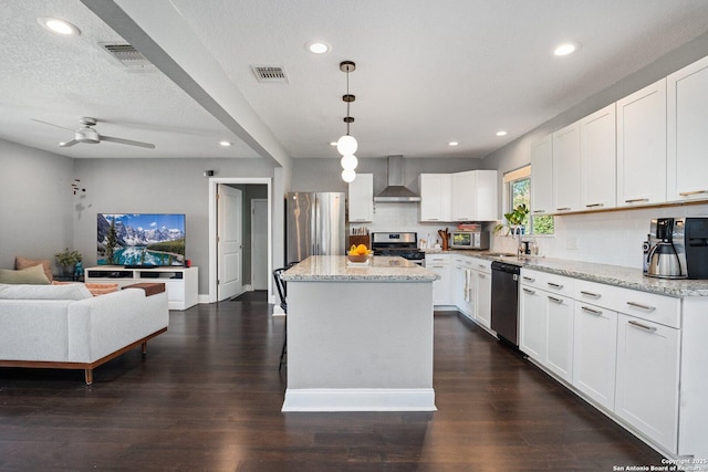 kitchen featuring white cabinetry, a center island, wall chimney exhaust hood, pendant lighting, and appliances with stainless steel finishes