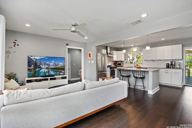 living room with a textured ceiling, ceiling fan, and dark hardwood / wood-style floors