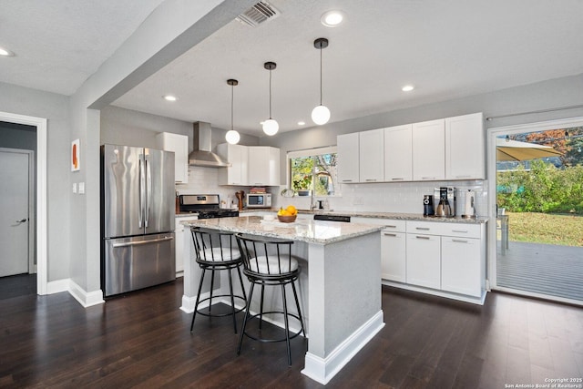 kitchen with stainless steel appliances, wall chimney exhaust hood, white cabinets, and pendant lighting