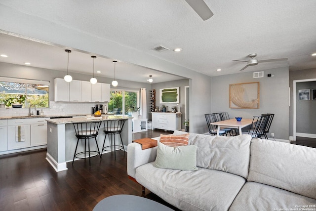 living room featuring sink, a textured ceiling, ceiling fan, and dark wood-type flooring