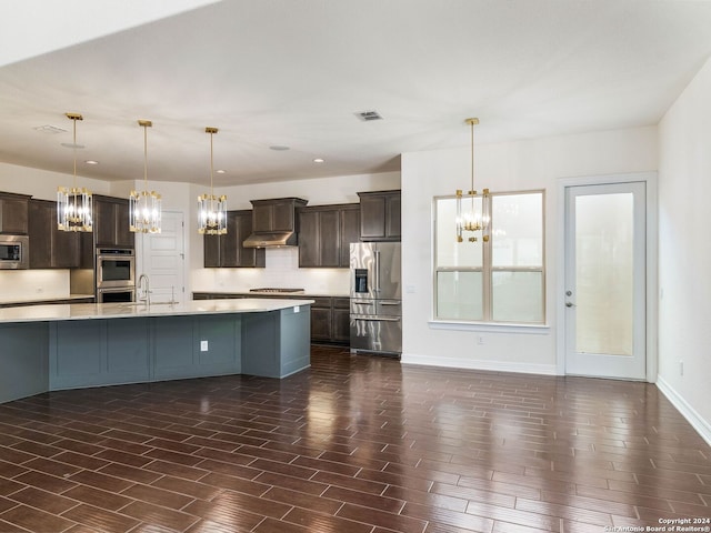 kitchen featuring wall chimney exhaust hood, decorative backsplash, dark brown cabinetry, pendant lighting, and appliances with stainless steel finishes