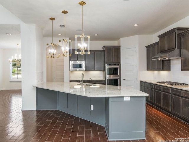 kitchen featuring stainless steel appliances, sink, decorative backsplash, hanging light fixtures, and light stone countertops