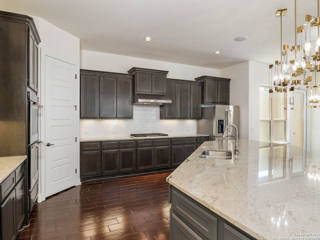 kitchen featuring appliances with stainless steel finishes, hanging light fixtures, light stone countertops, sink, and tasteful backsplash