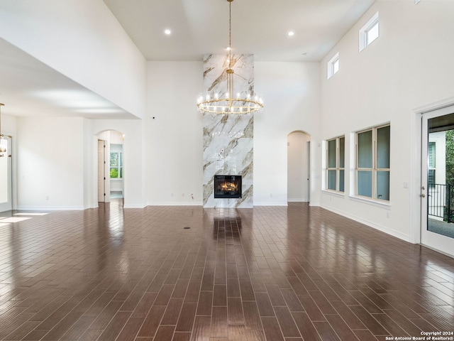 unfurnished living room with a high ceiling, a premium fireplace, an inviting chandelier, and a wealth of natural light