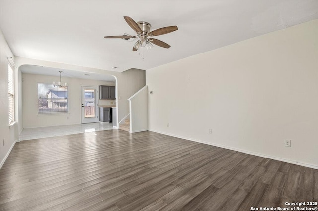 unfurnished living room featuring ceiling fan with notable chandelier and dark wood-type flooring