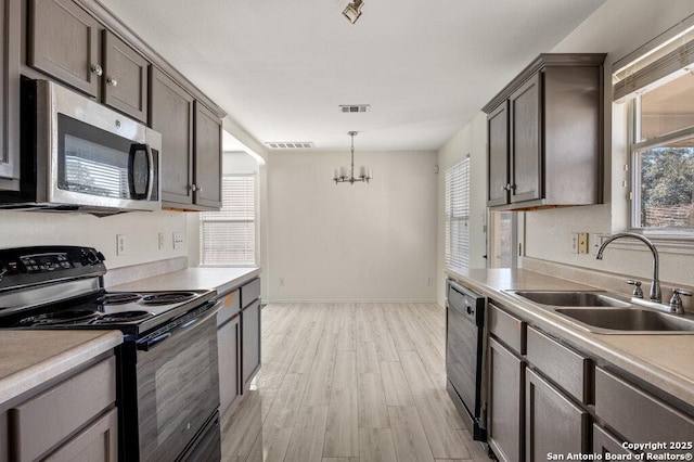 kitchen featuring a chandelier, black appliances, light wood-type flooring, pendant lighting, and sink