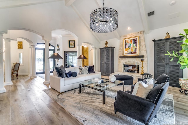 living room with a notable chandelier, high vaulted ceiling, a fireplace, light hardwood / wood-style flooring, and decorative columns