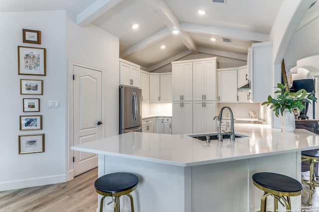 kitchen featuring white cabinets, a kitchen breakfast bar, vaulted ceiling with beams, and stainless steel refrigerator