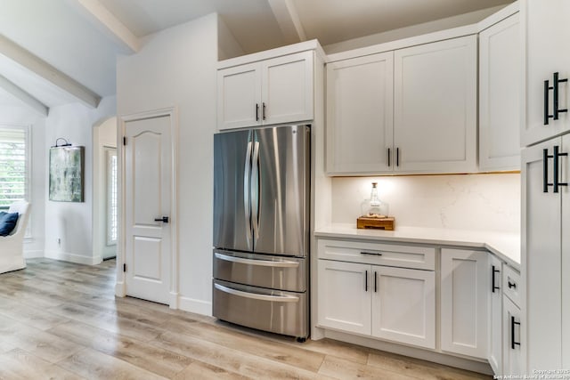 kitchen featuring white cabinetry, vaulted ceiling with beams, light wood-type flooring, stainless steel refrigerator, and backsplash