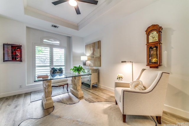 office space featuring a raised ceiling, ornamental molding, ceiling fan, and light hardwood / wood-style flooring