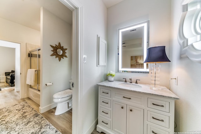 full bathroom featuring enclosed tub / shower combo, hardwood / wood-style floors, vanity, and toilet