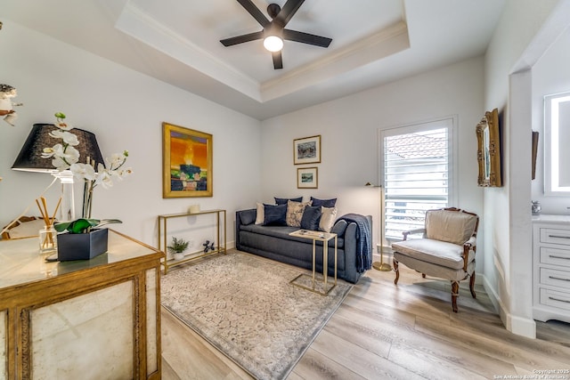 living room featuring light wood-type flooring, ornamental molding, a raised ceiling, and ceiling fan