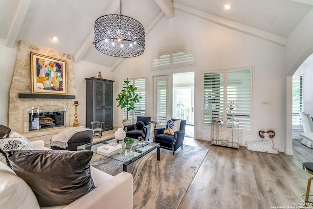 living room featuring a chandelier, high vaulted ceiling, wood-type flooring, beamed ceiling, and a stone fireplace