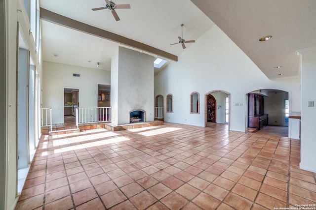 unfurnished living room with a high ceiling, a fireplace, ceiling fan, and beamed ceiling