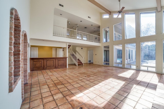 unfurnished living room with a high ceiling, beam ceiling, and ceiling fan