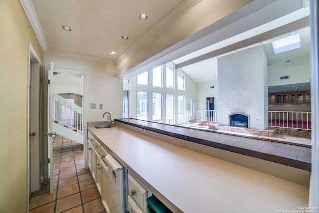 kitchen with sink, light tile patterned floors, a large fireplace, and vaulted ceiling with skylight