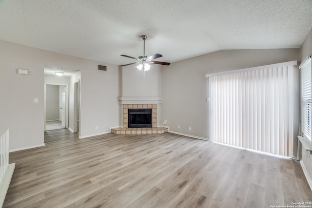 unfurnished living room with a textured ceiling, a tiled fireplace, lofted ceiling, and light hardwood / wood-style floors