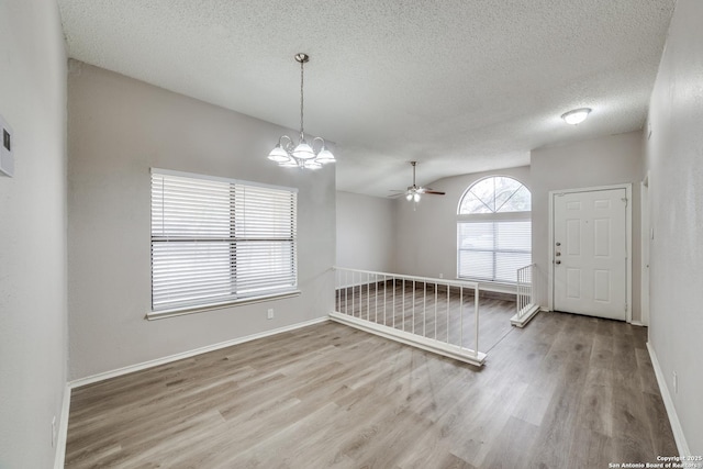 unfurnished room with ceiling fan with notable chandelier, wood-type flooring, a wealth of natural light, and vaulted ceiling